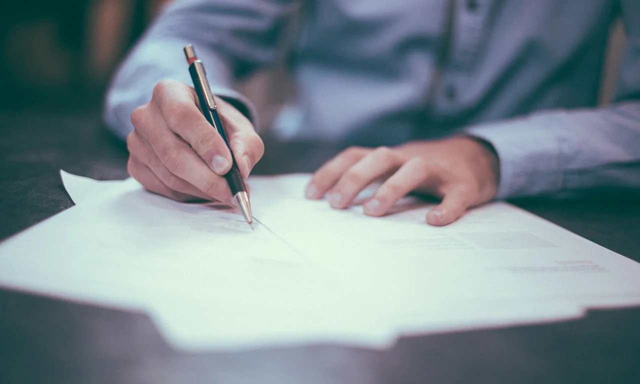 Une main rédigeant un testament olographe au stylo sur une feuille blanche